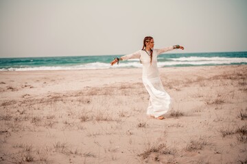 Model in boho style in a white long dress and silver jewelry on the beach. Her hair is braided, and...