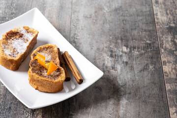 Traditional homemade Spanish torrijas decorated with cinnamon and Orange peel on wooden table. Copy space
