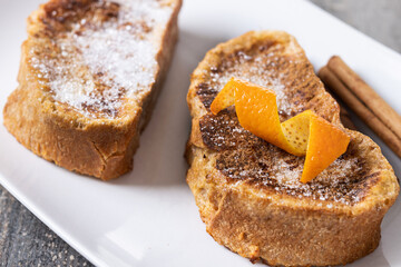 Traditional homemade Spanish torrijas decorated with cinnamon and Orange peel on wooden table
