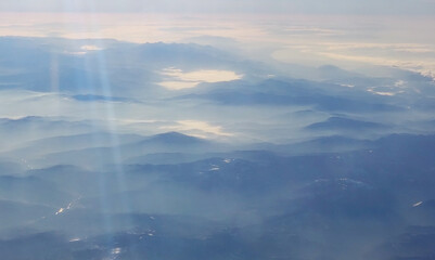 Fototapeta na wymiar View of the mountains in the fog at dawn from the airplane window. Beautiful wallpaper.