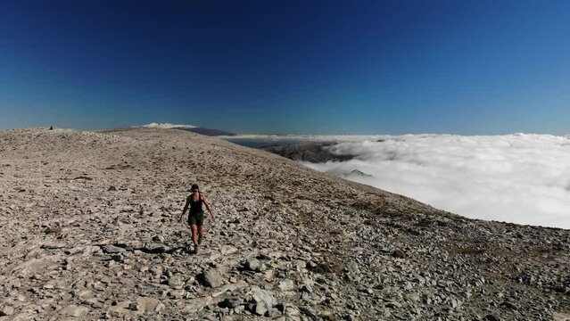 4K drone footage over woman walking on a rocky peak with sea of clouds and mountain range on the back at La Maroma summit, Malaga, Spain.
Mid angle, traveling movement.