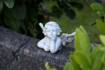 Kleiner Engel auf einem Grabstein zwischen grünen Blättern auf dem Friedhof