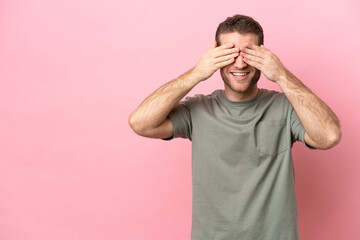 Young caucasian man isolated on pink background covering eyes by hands and smiling