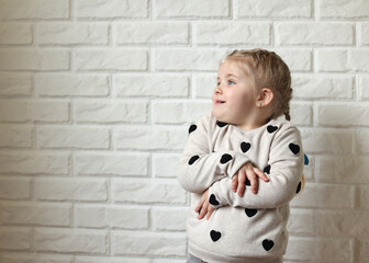 Funny child on a white brick background. A little girl poses in front of the camera