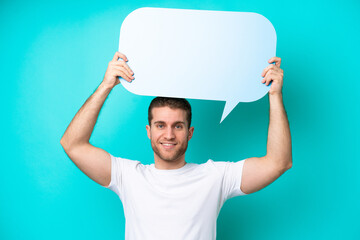 Young caucasian man isolated on blue background holding an empty speech bubble