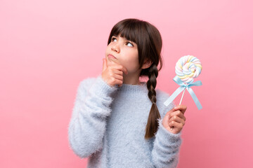 Little caucasian girl holding a lollipop having doubts