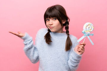 Little caucasian girl holding a lollipop having doubts while raising hands