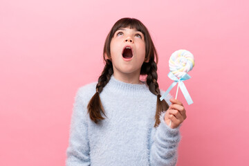 Little caucasian girl holding a lollipop looking up and with surprised expression