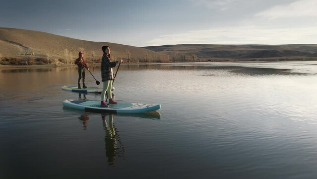 Two active girls walks on standup sup paddle boards at calm mountain lake