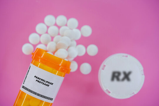 Pancrelipase Protease Rx medicine pills in plactic vial with tablets. Pills spilling   from yellow container on pink background.