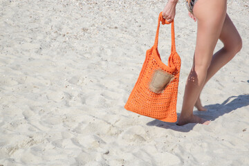 Tourist woman carrying bright orange crochet tote bag at sand beach
