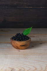 Fototapeta na wymiar Fresh ripe elderberry in a wooden bowl on a wooden background side view. Wild berries.