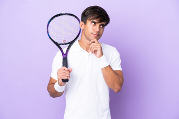 Handsome young tennis player man isolated on ocher background having doubts and thinking