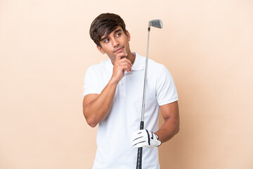 Young golfer player man isolated on ocher background and looking up