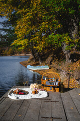 A cozy picnic setup by the lakeside features a woven basket filled with snacks and refreshments. Vibrant autumn leaves surround calm waters, creating a peaceful escape.
