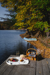 A cozy picnic setup by the lakeside features a woven basket filled with snacks and refreshments. Vibrant autumn leaves surround calm waters, creating a peaceful escape.