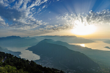 Dazzling sun in the evening sky illuminates all the peaks of the Balkan Montenegrin mountains and the coast of Kotor Bay