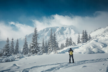 Incredible winter nature landscape. Alone man in snow covered mountain. Hiker, photographer on the or alpiniston run training outdoors active fit lifestyle. Snowy mountain scenery with snowfall