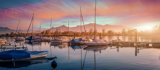 Scenic nature landscape. Sunrise on Chiemsee with vivid sky. Sailboats in the harbor on a summer...
