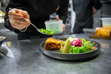 chef hand preparing Meat Pie with mashed potato and salad on restaurant kitchen