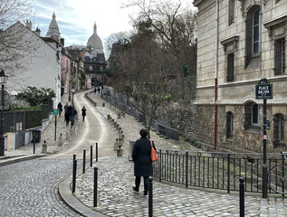 Frau mit Handtasche in Orange spaziert an einem trüben Tag am Place Dalida durch die Straßen von...