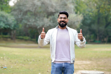 Young and confident indian man showing thumps up at park.