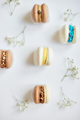 Top view set of different french cookies macaroons, cake macarons with flowers on white background, colorful almond cookies, pastel colors.