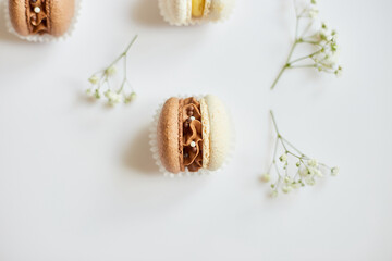 Top view set of different french cookies macaroons, cake macarons with flowers on white background, colorful almond cookies, pastel colors.