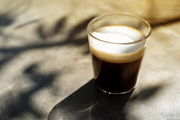 A cup of americano macchiato coffee  with  shadow of tree branch on desk  in the morning