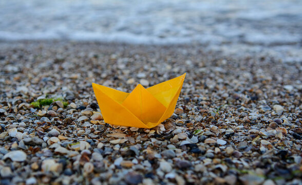 Yellow paper boat on the sea. Ship on seashells. Free place