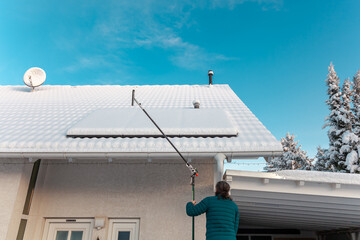 man will cleans the panel at rooftop from snow. removing snow off solar panels in winter. Removing...