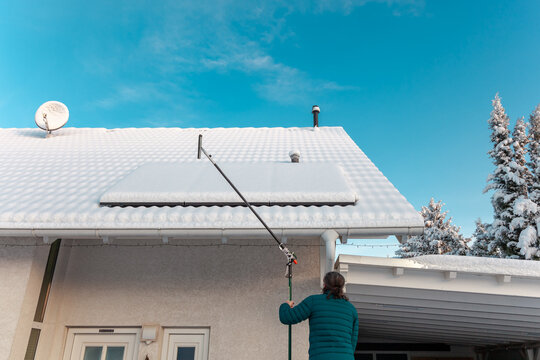 man will cleans the panel at rooftop from snow. removing snow off solar panels in winter. Removing snow photovoltaic system - solar cells. snow covers panels - no producing power. energy efficiency 