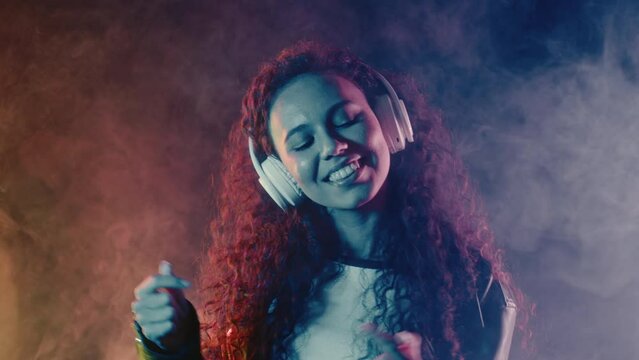 Positive woman listening music, singing, enjoying dance with headphone in smoke