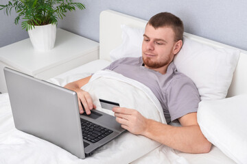 Man with laptop lying in bed. Online shopping without leaving home. Internet surfing. Gambling addiction. Cybersecurity. Black Friday sale. Cyber Monday. Online gift buy. Booking tickets hotels planes