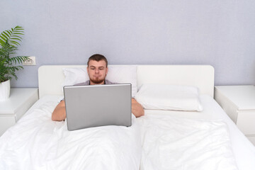 Man with laptop lying in bed. Freelancer works remotely from home. Distance education. Online shopping without leaving home. Internet surfing. Gambling addiction. Black Friday sale. Cyber Monday.