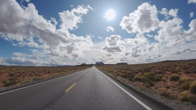 Drving down the highway with Arizona Monument Valley desert landscape in the foreground view with blue sky and white puffy clouds.