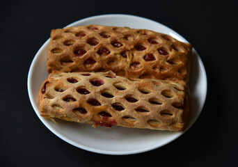 Sweet bun with jam on a white plate. Delicious bun with jam on a black background.