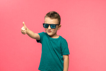 Pleasant satisfied boy shows thumbs up looking at camera, portrait. Attractive smiling boy in green casual t-shirt posing isolated on pink background. childhood, human emotions, lifestyle