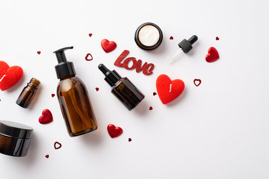 Valentine's Day presents concept. Top view photo of amber cosmetic bottles red heart shaped candles inscription love and confetti on isolated white background