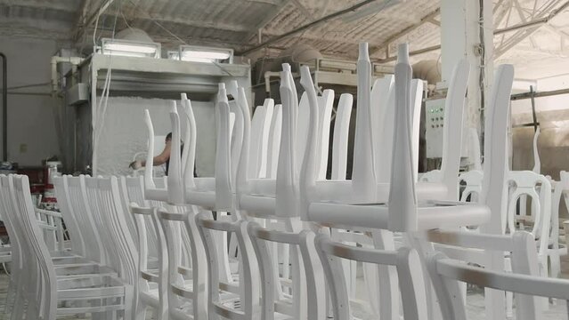 A worker painter paints wooden chairs