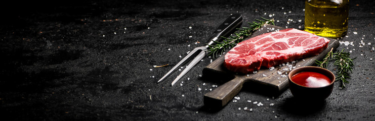 A steak of raw pork on a cutting board with tomato sauce and rosemary. 