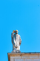 Front view, far distance of a carved, stone statue on corner of a 1300`s century building against a blue sky 