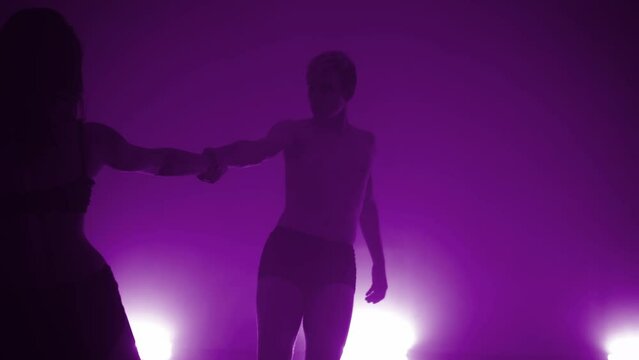 Close-up of elegant couple performing modern contemporary dance in darkness of studio