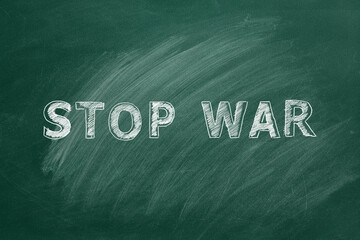 Lettering STOP WAR hand drawn in chalk on a school greenboard.
