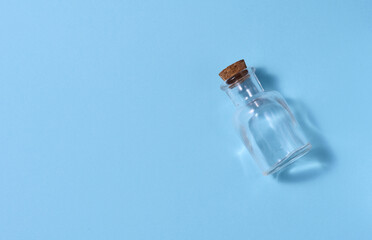 Empty glass bottle with cork on blue background, top view