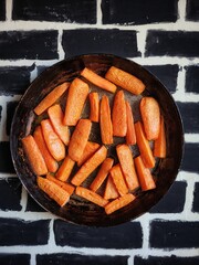 Caramelized carrot slices in a rustic frying pan on a black brick table. Top view of grilled vegetables.