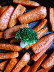 Close up of caramelized carrot slices and broccoli branch in a rustic frying pan. Top view of grilled vegetables.