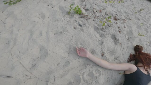 Dead body of a young woman lying on a sand of waistland. Killed unrecognizable  caucasian girl with long red hair dressed in black top. True crime concept 