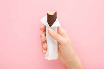 Young adult woman hand holding bitten dark brown chocolate bar with marzipan on light pink table...
