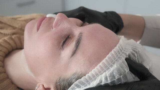 Profile portrait of relaxed woman's face, cosmetologist removes skincare product